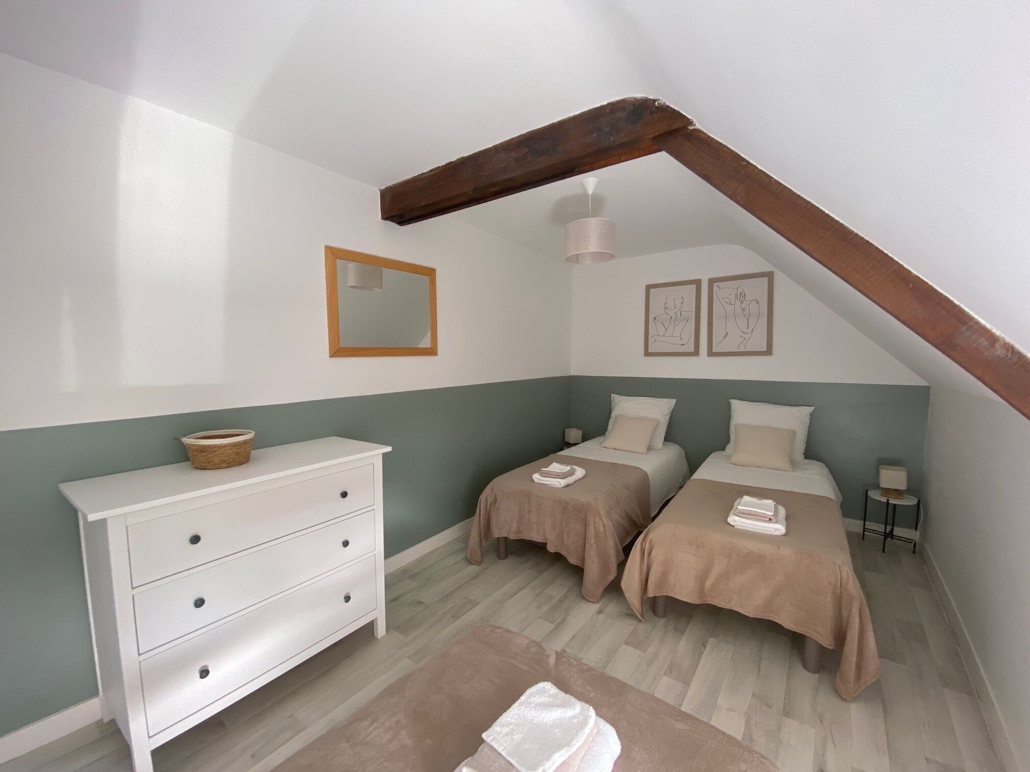 A bedroom with two beds, a dresser, a mirror, and artwork on the walls.