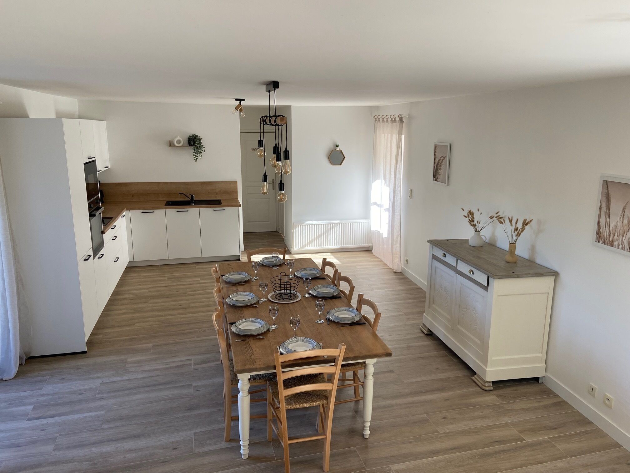 Una cocina moderna con armarios blancos, una mesa de comedor de madera para seis comensales, y una lámpara colgante.