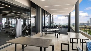 A modern gym with exercise equipment, large windows, and a view of the city. - Illovo Central 1023 (Sandton)