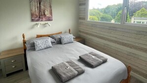 A bedroom with a large bed, a nightstand, a window with a view, and a painting on the wall. - Villa 19 Lanteglos 2 bed sleep 5 (Lanteglos)