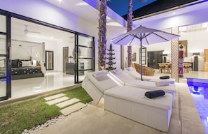Relax in a serene outdoor space with a wicker sofa set, pool, and lush greenery.