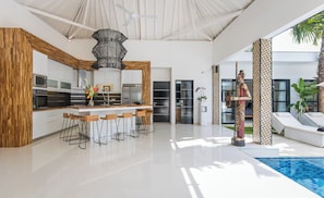 Relax in this spacious living area with a central kitchen island, decorative sculpture, and pool views.
