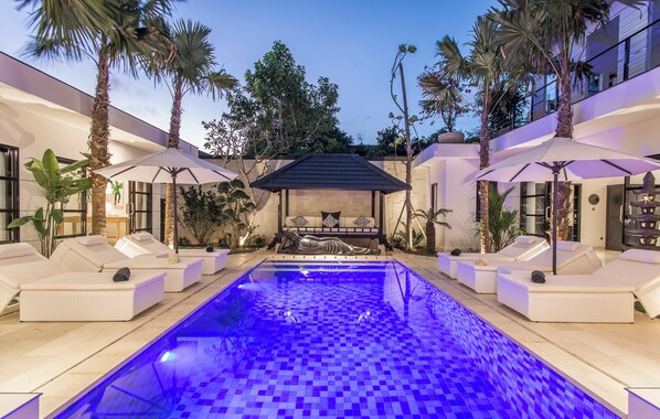 Relax by the pool surrounded by lush tropical plants and palm trees in a serene atmosphere.