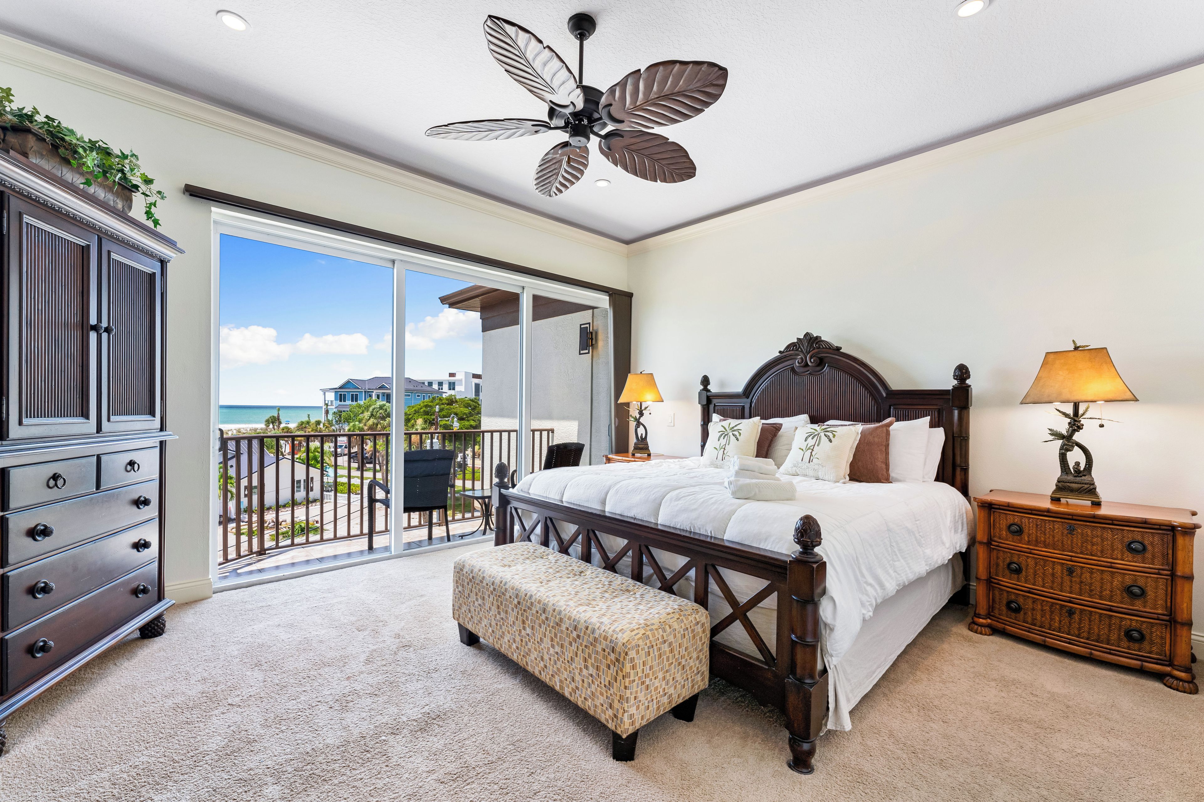 A bedroom with a large bed, a wooden dresser, a bench, and a ceiling fan.