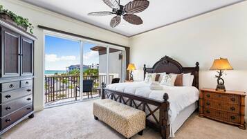 A bedroom with a large bed, a wooden dresser, a bench, and a ceiling fan.