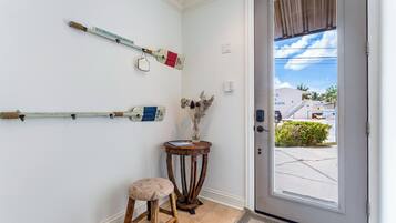 Una habitación con una puerta, un taburete, una mesita con un jarrón y objetos en la pared.