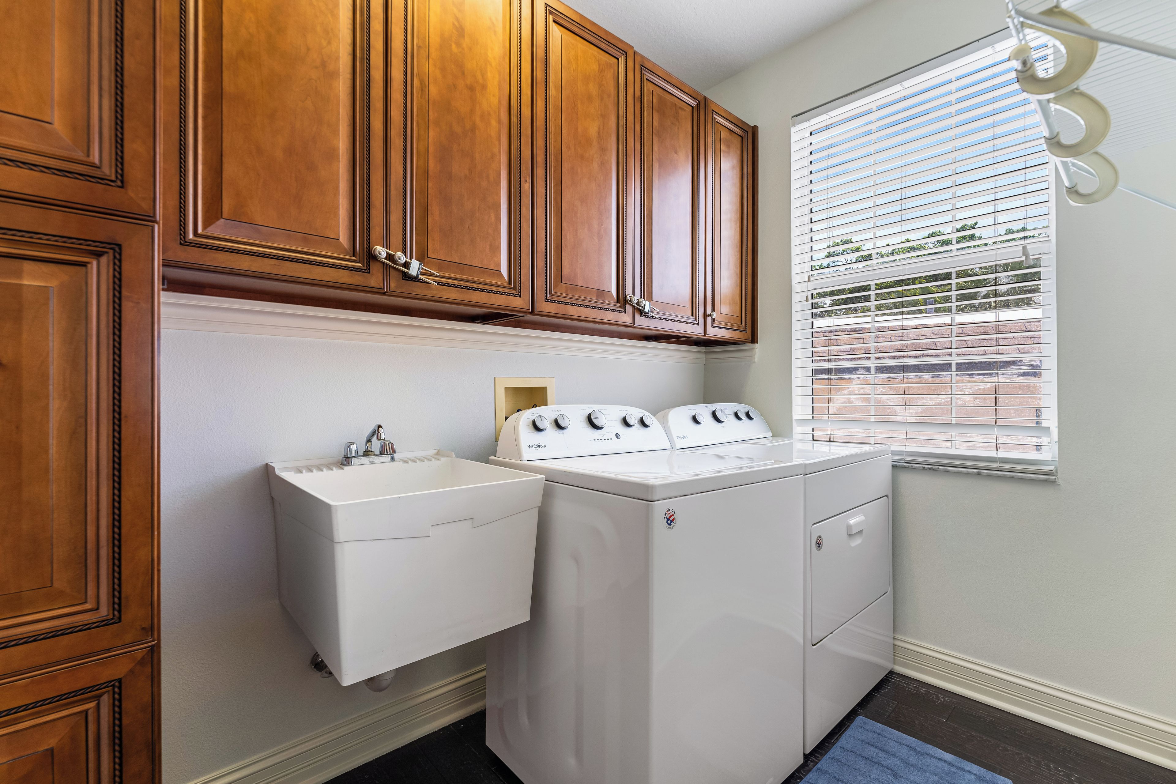 A laundry room with wooden cabinets, a white sink, and a front-loading washer and dryer.