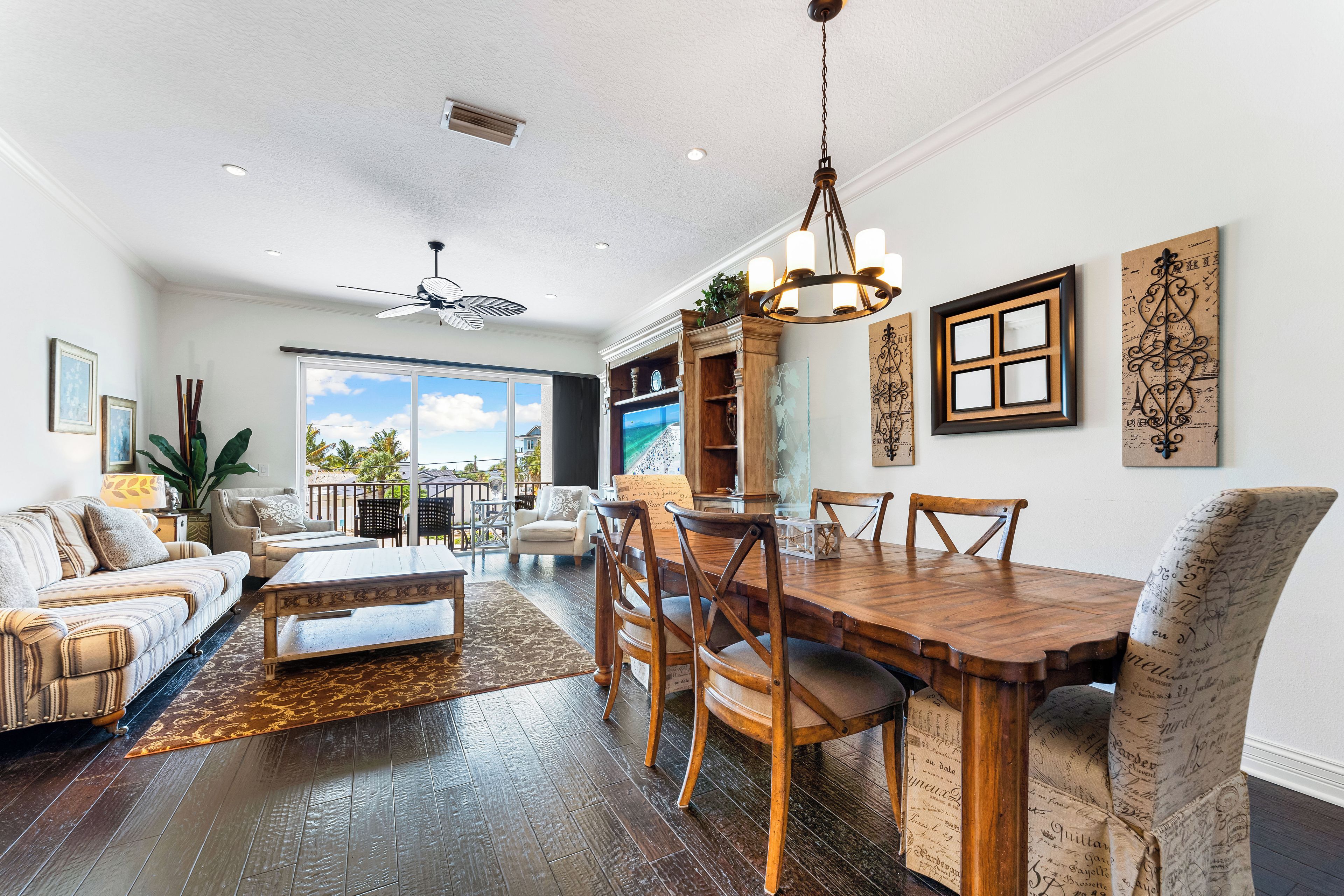 A spacious living room with a wooden dining table, comfortable seating, and a large window offering a view of the outdoors.