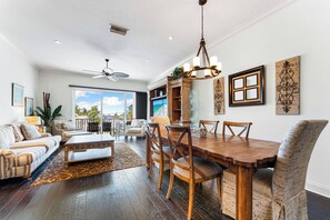 A spacious living room with a wooden dining table, comfortable seating, and a large window offering a view of the outdoors. - Beachside of the Village by Beachside (Siesta Key)