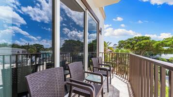 A balcony with wicker chairs and a glass table, overlooking a residential area with trees and houses.