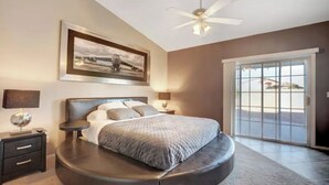 Une chambre à coucher avec un lit à la forme arrondie, un ventilateur de plafond, une grande fenêtre et un tableau encadré accroché au mur.