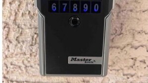 Un clavier numérique avec les chiffres de 0 à 9 et un symbole de cadenas, portant l’inscription « Master Lock », fixé sur un mur texturé.