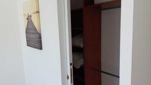 Una stanza con pavimento in legno, una porta bianca e un armadio con un letto e uno scaffale.