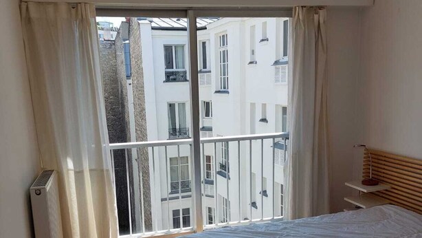 Una camera da letto con un'ampia finestra, pavimento in legno e un letto con biancheria bianca.