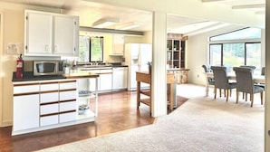 A spacious kitchen with white cabinets, a microwave, and a dining area with a table and chairs. - Lookout @ SeaAcres -Beach Access (San Juan County)