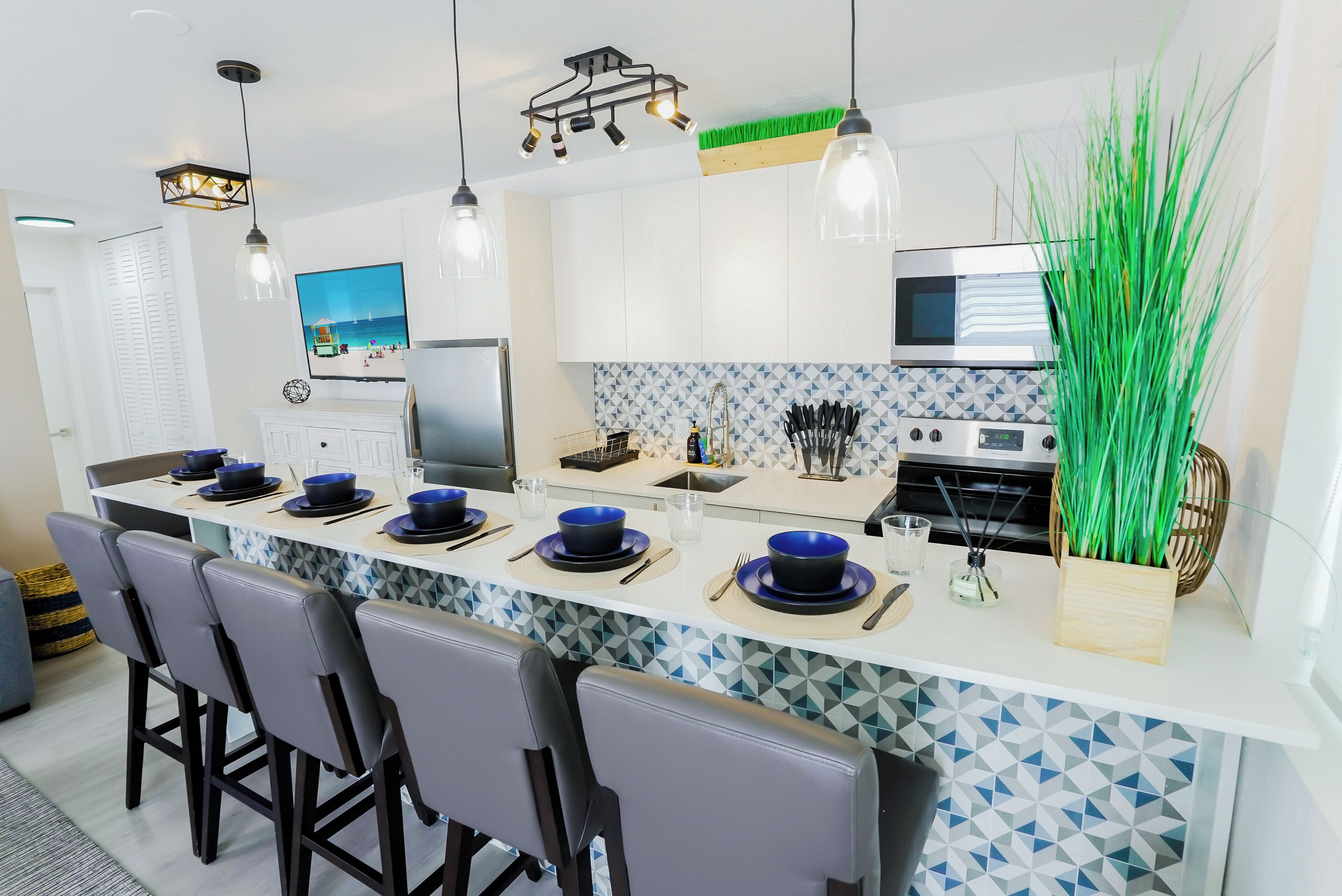 Una cucina moderna con isola centrale, mobili bianchi e una parete di fondo rivestita in piastrelle bianche e azzurre.