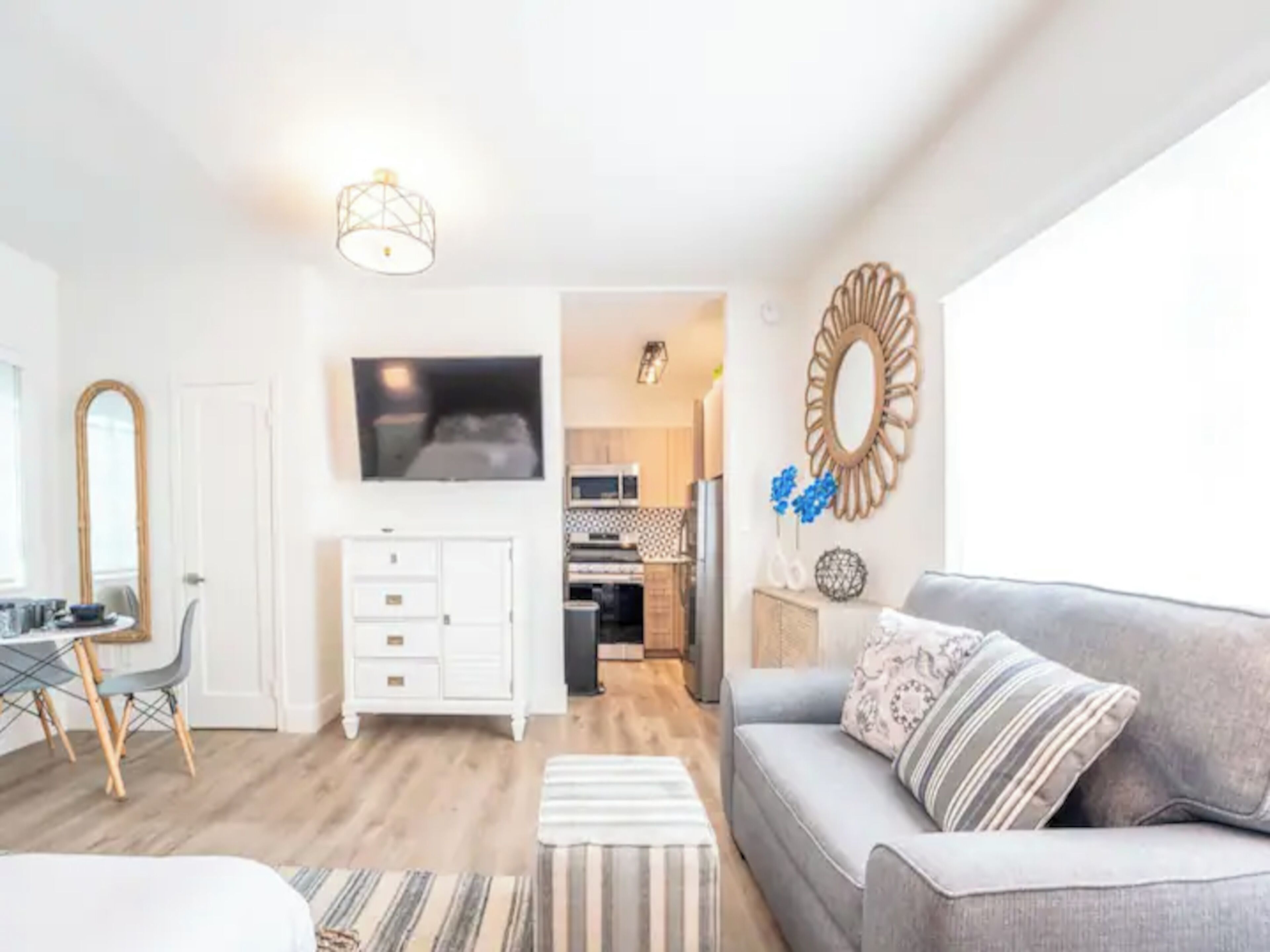 Un salon moderne avec un canapé gris, un téléviseur fixé au mur et un coin repas comprenant un buffet blanc et une chaise.