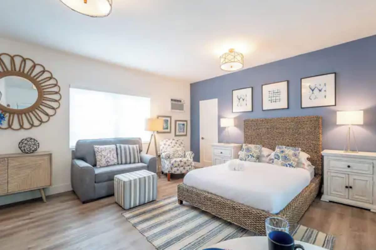 A bedroom with a large bed, a sofa, a chair, a bedside table, and a lamp.