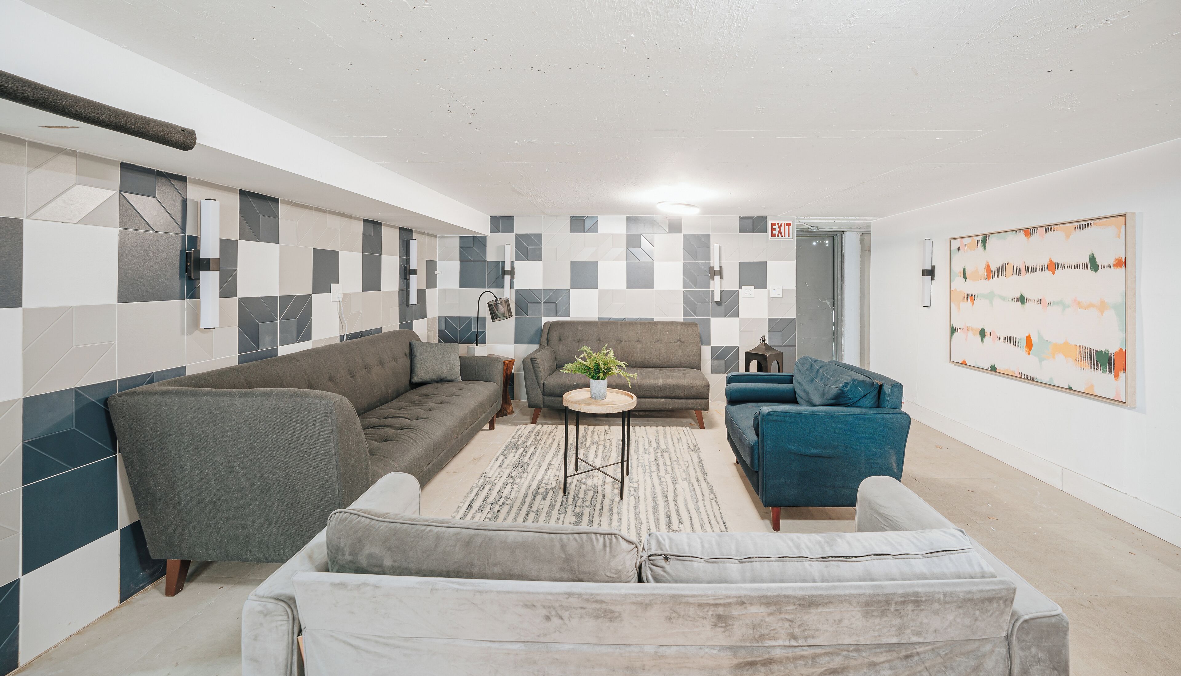 A modern living room with a grey sofa, a blue armchair, and a small round table with a plant.