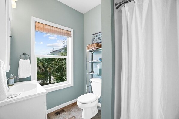 Un baño con ventana, inodoro, lavamanos y cortina de ducha.