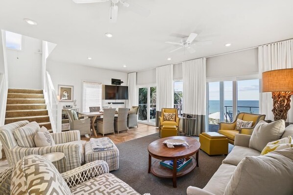 A spacious living room with a staircase, a dining area, and a view of the ocean. - Beachfront, 2 Screened-In Decks, Meticulously Maintained in San Blas Estates (Cape SanBlas)