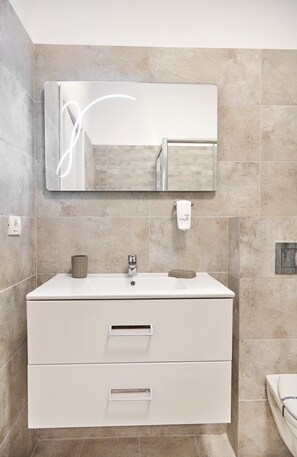 A modern bathroom with a large mirror, a white vanity with two drawers, and a toilet.