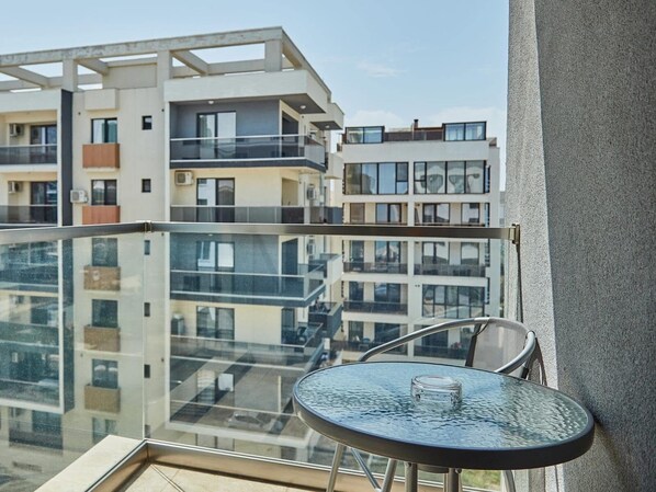 A modern apartment with a glass balcony, a round table, and a view of other buildings.