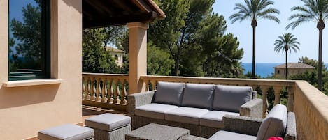 A balcony with wicker furniture, a view of the sea, and palm trees.