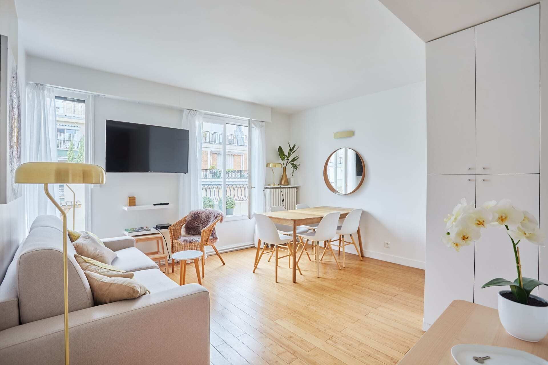 A modern living room with a sofa, dining table, chairs, a TV, and a balcony view.
