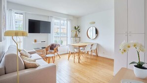 A modern living room with a sofa, dining table, chairs, a TV, and a balcony view. - Degas Appart 1 - Two Bedroom Apartment, Sleeps 6 (Paris)