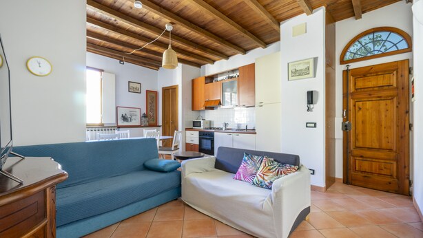 A living room with a blue sofa, a white sofa, and a wooden ceiling. There is a kitchen in the background with wooden cabinets and a stove. - Faenza 91 Apartament (Firenze)