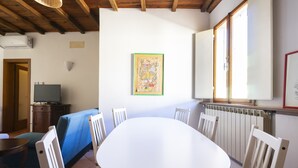 A room with a round table, white chairs, a sofa, and a television. - Faenza 91 Apartament (Firenze)