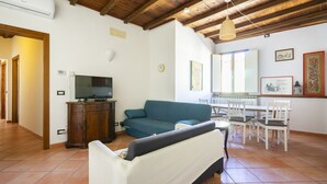 A living room with a sofa, television, wooden ceiling, and a dining area with chairs and a table. - Faenza 91 Apartament (Firenze)