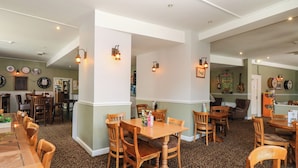 A spacious dining area with wooden tables and chairs, a bar area with stools, and a kitchen visible in the background. - 42 Valley Lodge (Gunnislake)