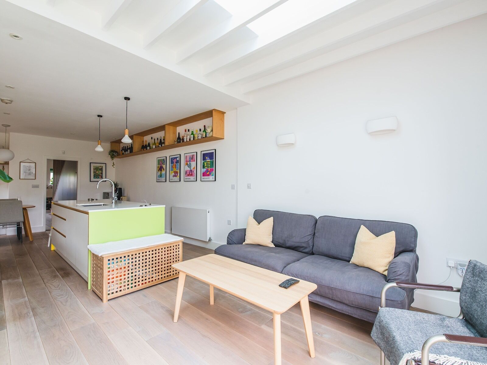 Un espacio habitable moderno con un sofá gris, una mesa de centro de madera y una cocina con encimera blanca y estanterías de madera.