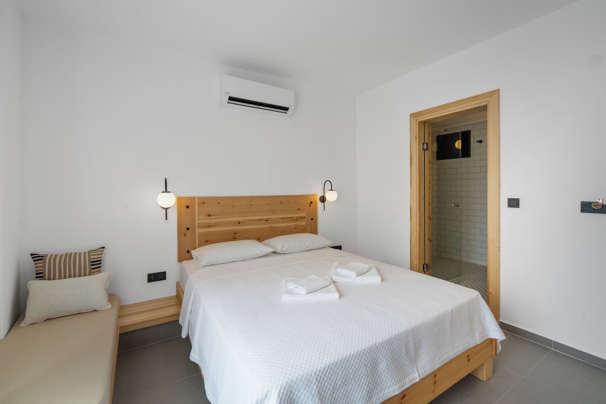 Un dormitorio con cabecera de madera, ropa de cama blanca y una mesita de noche pequeña.