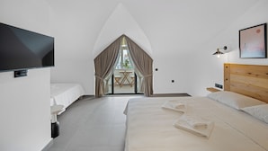 Une chambre d’hôtel moderne avec un grand lit, une télévision, une petite table et une vue sur l’extérieur, visible à travers une fenêtre avec des rideaux.