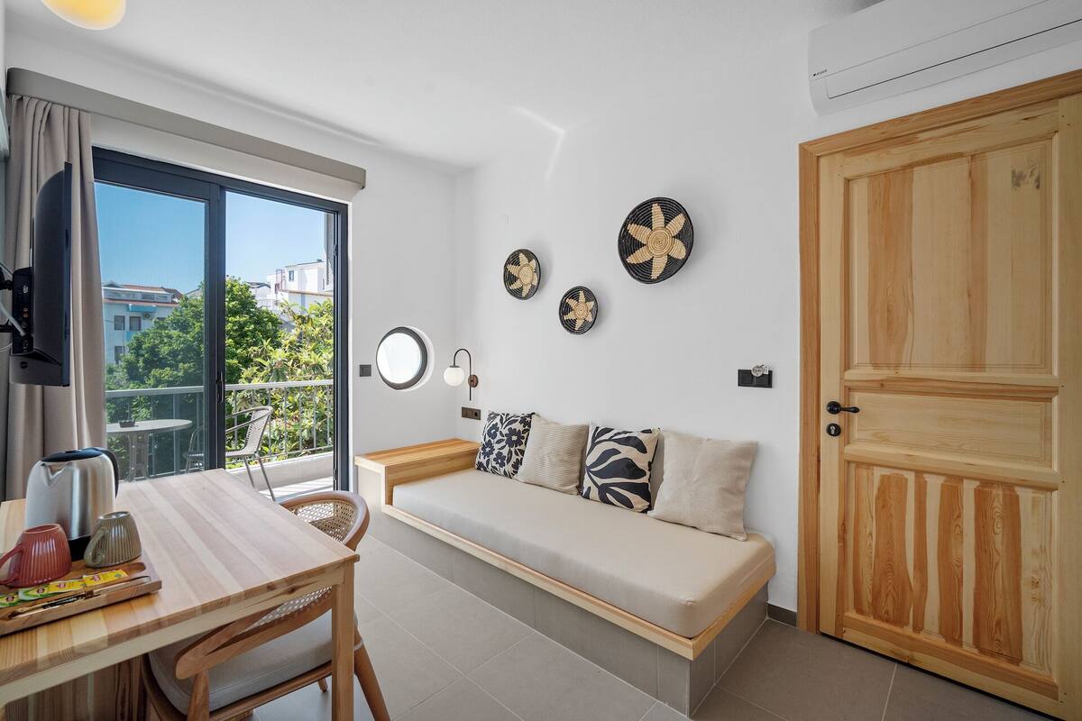 Una sala de estar moderna con un sofá, una mesa de comedor y un balcón con vistas a edificios y árboles.