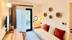 Une pièce de taille modeste, avec un bureau en bois, un canapé agrémenté de coussins rouges, un téléviseur et un luminaire fixé au mur.