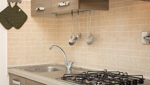 A kitchen with a gas stove, stainless steel sink, hanging pots, and a wooden backsplash.