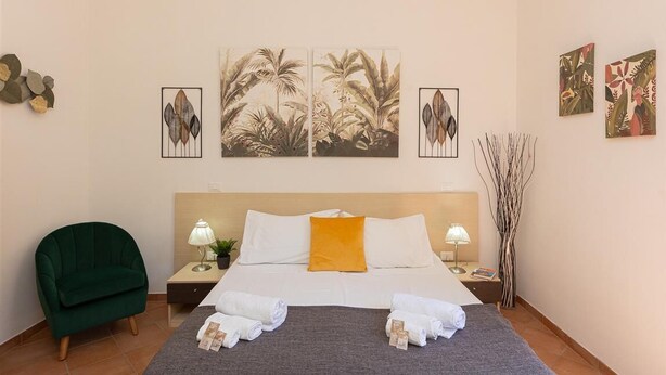 A hotel room with a bed, two nightstands, a green armchair, and artwork on the walls.