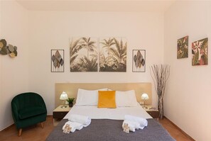 A hotel room with a bed, two nightstands, a green armchair, and artwork on the walls.