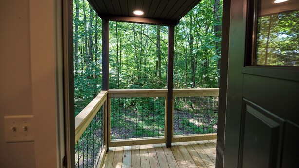 Eine Holzterrasse mit Metallgeländer, die auf einen Wald blickt.