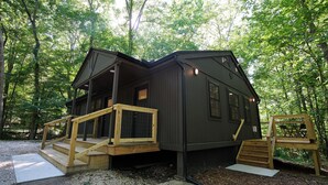 Eine Holzhütte mit einer Holztreppe, die zu einer Terrasse führt, umgeben von Bäumen.