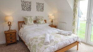 A bedroom with a bed, two nightstands, a radiator, and a view of the outdoors. - Turning Tide (Chathill)
