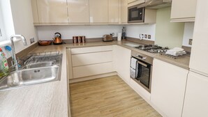 A modern kitchen with stainless steel appliances, wooden flooring, and light-colored cabinetry. - Turning Tide (Chathill)