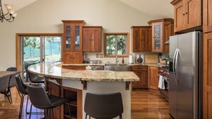 Una cocina con armarios de madera, un refrigerador de acero inoxidable, una encimera de granito y un ventanal con vistas a un patio trasero.