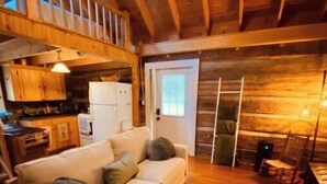L’intérieur chaleureux d’un chalet avec un canapé, un tapis à motifs, des murs en bois et un coin cuisine.