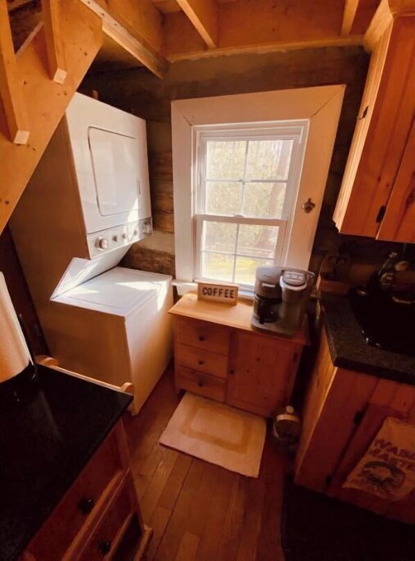 A compact kitchen with a washing machine, a coffee station, and a window with a view.
