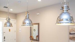 Ein Zimmer mit drei hängenden Pendelleuchten, einem Holzkonsolentisch mit Blumenvase und einem Spiegel an der Wand.